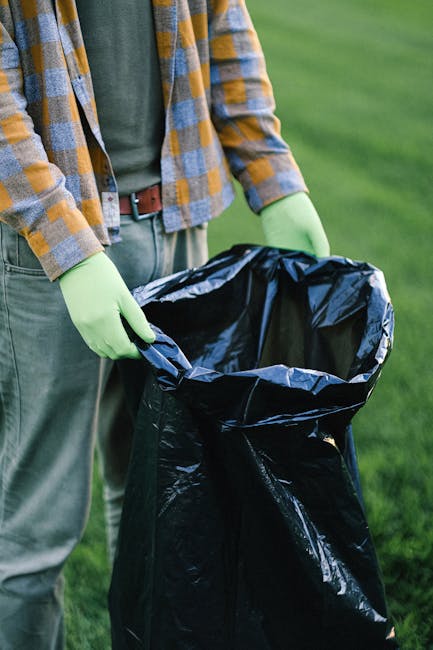 Four young people, two females and two males, are engaged in a litter-picking activity amidst a wooded area near a lake. They are dressed in casual outdoor clothing, including hats and t-shirts, with 